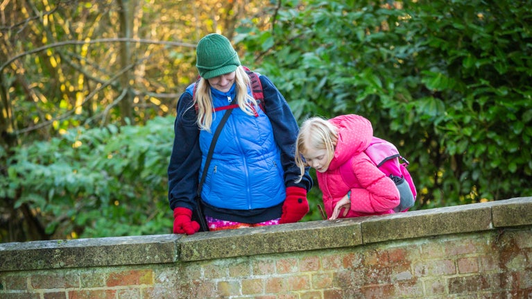 A woman and child play Pooh sticks on a bridge at Mottisfont in Hampshire
